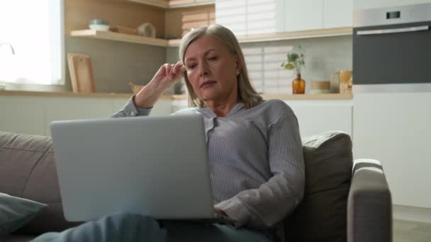 幸せな高齢者の白人女性は ラップトップの笑顔成熟した女性のブラウジングソーシャルネットワークを入力して自宅のソファで休んでリラックスインターネットでオンラインショッピングをチャット映画の使用コンピュータアプリ — ストック動画