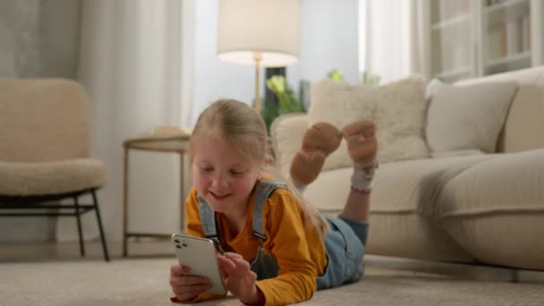 Küçük Beyaz Kız Çocuk Oturma Odasında Uzanıyor Mobil Online Oyunlar — Stok video