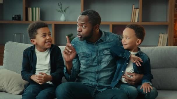 在家里的非洲裔美国家庭单身父亲和两个孩子爸爸沉默沉默的样子听着手指悄悄地叹息小儿子在沙发上打爸爸吵吵闹闹的孩子们的行为问题 — 图库视频影像