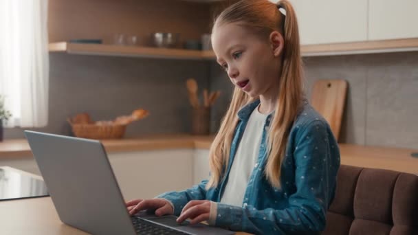 白种人可爱的小女孩小女儿小女儿学校学生女学生使用笔记本电脑打字使用电脑小玩意成瘾的一代电子学习学习在家里厨房玩电子游戏 — 图库视频影像