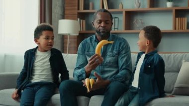 Afro-Amerikan ailesi evde iki çocuklu bekar baba çocuklarla konuşuyor meyve vitaminleri veriyor sağlıklı yiyecek saymayı öğretiyor organik gıda yiyor çocuk bakımı yapıyor.