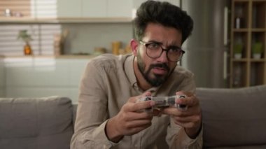 Arap Hintli erkek oyun bağımlılığı TV 'de oyun konsolu oyunu oynuyor ev mutfağındaki kanepede kumandanla oyun oynuyor oyun kaybetmekten rahatsız olan oyuncu hayal kırıklığına uğradı.