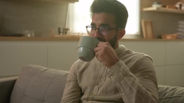 リラックスした穏やかな夢アラビア人男性満足男リラックスソファに自宅でお茶を飲みながら朝のコーヒーキッチンで飲み物を楽しむ良い残りの部分だけで一時停止週末を考える香りの飲み物のカップを作る — ストック動画