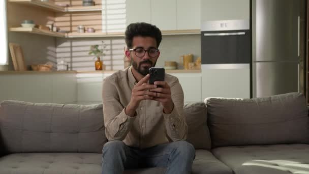 アラビア系インド人男性キッチンで携帯電話を使用してスマートフォンのストレスを置く無料呼吸と瞑想上のソファヨガの練習名前味リラックス健康的な考え方禅穏やかな瞑想精神的な意識 — ストック動画