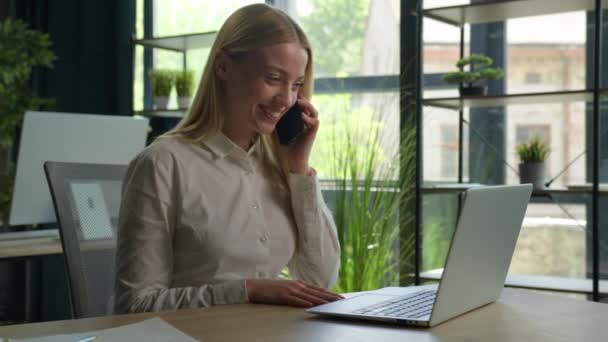 幸せな白人興奮した女の子実業家の話携帯電話ビジネスプロジェクトの女性相談クライアントの呼び出し携帯電話オフィスでノートパソコンを使用します — ストック動画