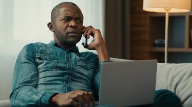 Ciddi Afro-Amerikalı bir adam ev etnik işadamının bilgisayarında telefonla konuşuyor. Cep telefonuna cevap veriyor. Telefonları kullanarak uzaktan internet çözme sorunları yaşıyor.