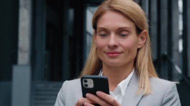 Kafkas kadın işkadını işkadını işveren sosyal ağı tarıyor cep telefonuyla dışarıda ofis binasının yanında yürüyor bayan girişimci e-posta mesajlarını kontrol ediyor.