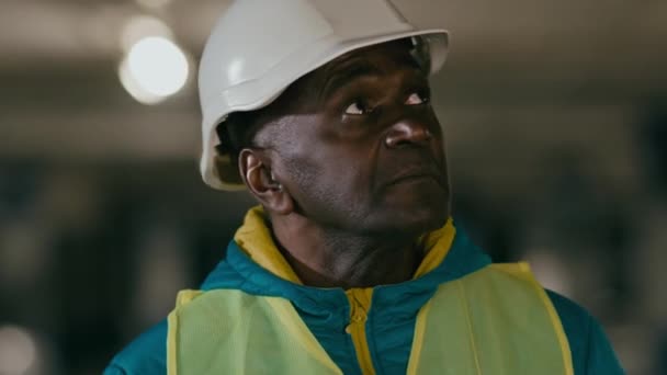 アフリカ系アメリカ人の男性の建築家の検査官保護ヘルメットの開発者は地下駐車場を検査エンジニアリング事業計画を熟考と思う男性プロのフォアマン製造作業をチェック — ストック動画