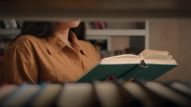 ブックケース近くの大学図書館で本を読む認識できない女性スマート女子大生教師読書教科書文学は 本棚の本を介して宿題ビューを勉強するための準備 — ストック動画