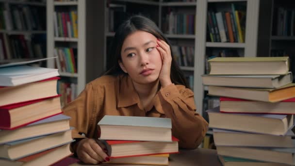 悲しい疲れた女の子学生退屈で机の上に本で大学図書館怠惰なやる気のないアジアの女性準備のために困難な大学の試験の宿題感じ疲れ退屈な研究愛情のない科目 — ストック動画