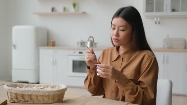 中国女孩在家里的厨房里吃着健康的天然酸奶亚洲女人在家里吃着甜点早餐一位饥饿的女士吃着蛋白质酸奶减肥保健品 — 图库视频影像