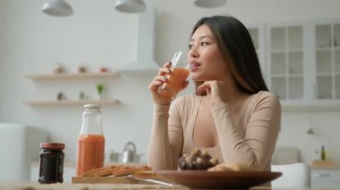 Asyalı gülümseyen Koreli kadın Koreli ev hanımı anne karısı portakal suyu içiyor, şeftali suyu içiyor kokteyl içiyor taze meyve suyu içiyor vitaminli sağlık ürünleri dağıtıyor ev mutfağında kahvaltının tadını çıkarıyor.