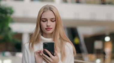 İş merkezinde yürüyen beyaz bir kadın odaklanmış kız öğrenci müşteri akıllı telefonuyla yürüyor. İnternetteki mobil uygulama kaygısız bayan müşteri telefon cihaz bağımlılığında sohbet mesajı gönderiyor.