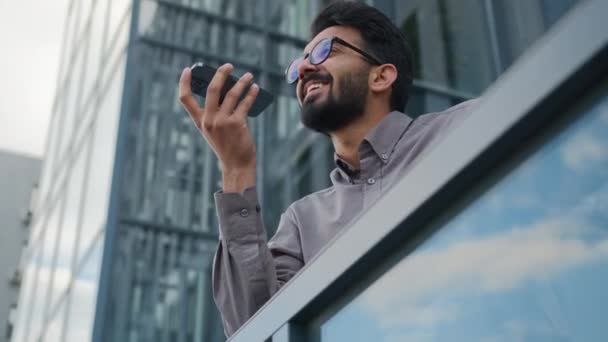 幸せな笑顔インドの男性実業家ビジネス雇用者男は電話で音声メッセージを記録します音声チャットAiモバイル支援を使用してマイクでボイスメールを指示市内のスマートフォントークスピーカーを話す — ストック動画