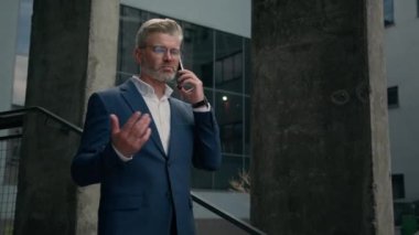 Şehir merkezinde başarılı bir kıdemli adam yürüyor şirket binası yakınlarında merdivenlerden iniyor ofis toplantısına gidiyor cep telefonu görüşmeleri yapıyor açık hava iş projeleri hakkında konuşuyor cep telefonuyla konuşan eski bir işadamı.