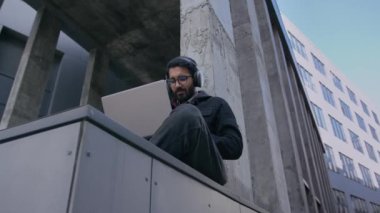 Hintli üniversite öğrencisi kulaklık takıyor. İş adamı Webinar ya da uzak bir sınıfta açık hava Arap erkek işadamı. Şehirde ofis binasının dışında dizüstü bilgisayarla çalışıyor.