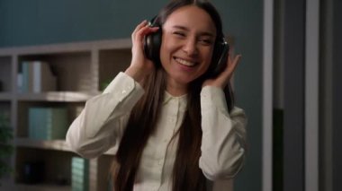 Dertsiz gülümseyen Kafkasyalı iş kadını kulaklıklı kadın ofis çalışanı müziği dinle müdür gülümse favori dans eden iş kadını mutlu kulaklıkla müzik dinlemekten zevk al.