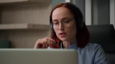 Kulaklıklı beyaz bir iş kadını müşterilerle iletişim kurar. Kadın ofis çalışanlarının sorunlarını çözer. Laptop bilgisayarıyla video konferansı yapar. Ciddi iş kadını konuşuyor. Web kamerasından uzak sohbet.