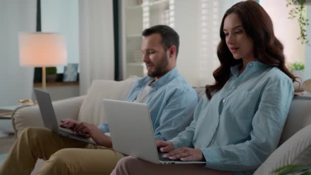 幸せな現代家族白人カップルにソファソファ使用デバイス男女性夫妻ブラウジングラップトップコンピュータにホーム人々ガジェット中毒技術中毒見ますお互い笑顔 — ストック動画