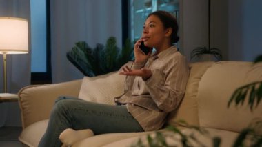 Gülümseyen Afrikalı Amerikalı mutlu kız gece evde cep telefonuyla konuşuyor. İnternetten yemek siparişi veriyor. Kanepede iletişim kuruyor.