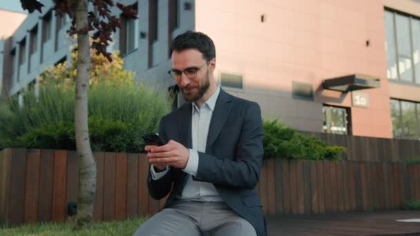 市内の携帯電話でメッセージを入力する白人実業家男性リーダー労働者雇用者ソーシャルネットワークを閲覧スマートフォンアプリを使用して笑顔のビジネス起業家オフィス外カメラの笑顔を見て — ストック動画