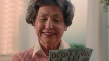 Happy Caucasian grandmother counting money at home excited senior woman holding cash old female granny elderly retired lady hold count banknotes financial lottery prize reward salary savings wealth