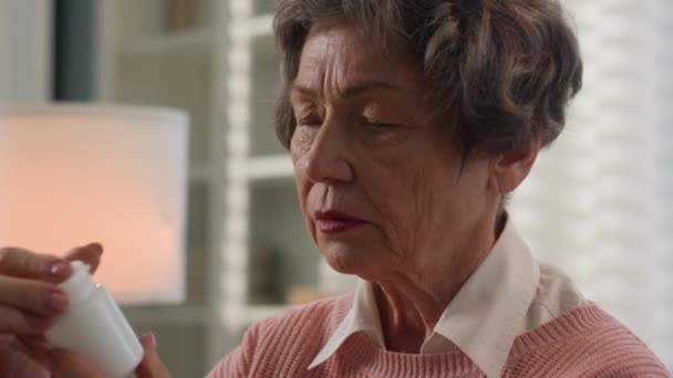 自宅で古い女性高齢者のおばあちゃんの引退した女性は薬の瓶を保持する薬用量の鎮痛剤の読書名 アルツハイマー病の医療の概念 — ストック動画