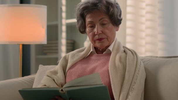 严重不满意的白种人老妇人年事已高的老太太盖着毯子安详的老年妇女退休的中年老奶奶在家里沙发上看书坏书喜欢读小说 — 图库视频影像
