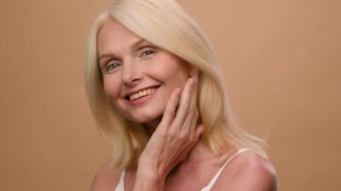 Portrait middle aged happy mature Caucasian woman senior 50s model flirty smiling at camera on beige studio background anti-aging beauty skin care procedures face lifting anti-wrinkle plastic surgery