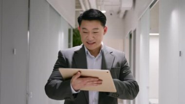Happy middle-aged Asian chinese korean businessman employer manager smiling man use digital tablet in office hall male entrepreneur browsing internet on device online business chat search social media
