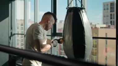 Active boxer sportsman in boxing gloves hitting punching bag intense box exercise motivated sport man fighter training fist punches blows in gym strength body workout maintain muscles masculine power