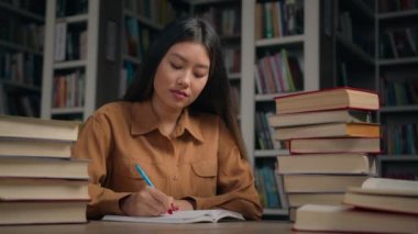 Üniversite kütüphanesinde kitaplarla ödev yapan zeki odaklı Asyalı kız öğrenci. Üniversite sınavına hazırlanan ciddi kız öğrenci. Bilimsel tarih projesi yaz.