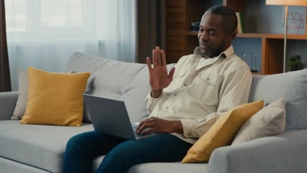快乐的非洲男人商人自由职业者在线教师用笔记本电脑在家里沙发上聊天远程商务会议与朋友聊天在虚拟会议上说远程话 — 图库视频影像
