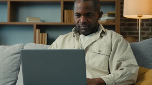 快乐的非洲裔美国商人 自由职业者 完成电脑工作 在家里紧密地使用笔记本电脑 干得很好 满意放松的男性 把双手放在头后面 放松地躺在舒适的沙发上 — 图库视频影像