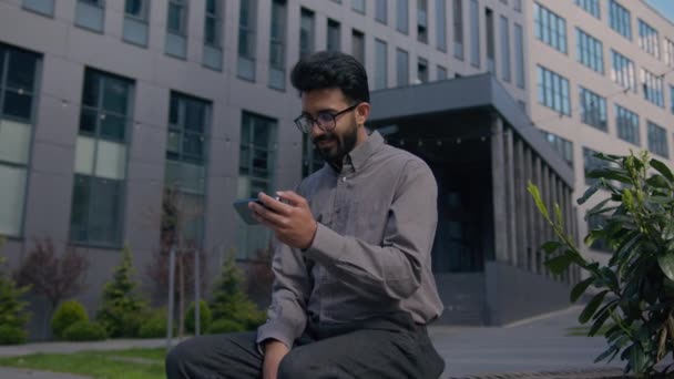 エキサイティングなインドのアラビア人男性のビジネスマンは スマートフォンでオンラインマッチを獲得する屋外の携帯電話上のビデオを見て 都市の幸せな男のオフィスの雇用主は 業績の成功を祝います — ストック動画