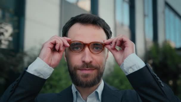 プロの実業家コーカサスの人間の都市肖像画成功したビジネス起業家雇用主の投資家は近代的なオフィスの近くのカメラの外で笑っている眼鏡の悪いビジョンを屋外に置くメガネを着ます — ストック動画