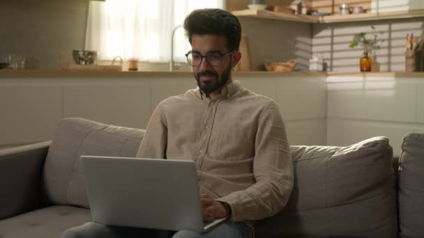 在家里工作的阿拉伯穆斯林自由职业者使用笔记本电脑技术快乐的商人在厨房沙发上满意地在线下单在家里大手大脚地打手势推荐好的服务 — 图库视频影像