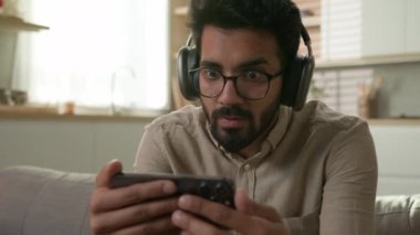 Hayal kırıklığına uğramış Arap Hintli adam cep telefonuyla maç seyrediyor. Mutfaktaki futbol maçını kaybettiği için üzgün. Kulaklıklı, cep telefonunda kötü sonuç kaybına bakan bir erkek.
