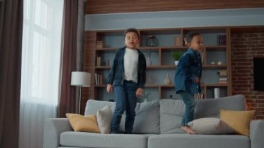 İki aktif yaramaz çocuk evdeki kanepede zıplayan Afrikalı Amerikalı hiperaktif kardeşler etnik çocuklar oturma odasında kanepeye atlayıp oyun oynarken eğleniyorlar.