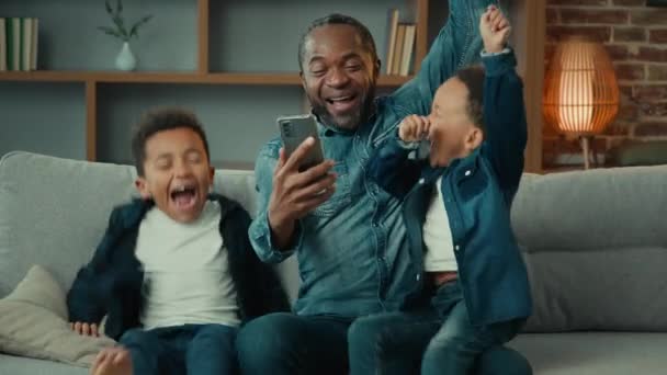 Coşkulu Afrikalı Amerikalı Baba Çocuklu Çocuklar Kanepeye Oturup Telefon Kazanan — Stok video