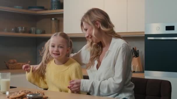 カカシアの幸せな家族の母性面白いかわいい子供の少女はキッチンでダイニングテーブルで母親と座って手を握り 子供の娘と一緒に腕で音楽ダンスに動く — ストック動画