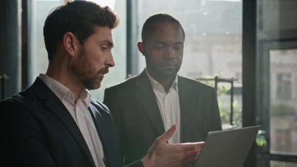 日当たりの良いオフィスにコンピュータを持つ2人の多種多様なビジネスマン オンラインプレゼンテーションビジネスを示すラップトップを持つコーカサスビジネスマンコンサルタントエージェントトレーダー アフリカ系アメリカ人男性クライアント — ストック動画