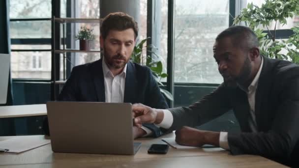 2人の多種多様なビジネスマンがオフィスでノートブックを書くオンラインデータプロジェクトについて話し合います コーカサス人のビジネスマンとアフリカ系アメリカ人の同僚 一緒に働く男性 — ストック動画