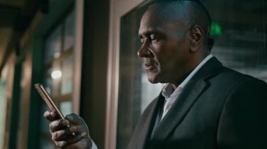 Yakın plan gülümseyen mutlu Afro-Amerikalı adam cep telefonuyla e-posta taraması yapıyor. Mesajları kontrol ediyor. Akıllı telefon etnik işadamının cep telefonuyla yaptığı telefon görüşmesinde iyi haber sosyal medya ağı okuyor.