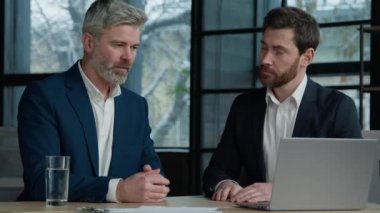 İki beyaz erkek iş ortağı online başlangıç dizüstü bilgisayarını tartışıyorlar. Satış elemanı el sıkışıyor. Müşteri temsilcisi, ofis ortaklığındaki yatırımcı el sıkışma yatırımcılarına danışıyor.