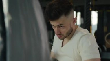 Aktif motivasyona sahip erkek boksör boks antrenmanı spor salonunda kum torbasıyla yorgun beyaz adam spor kulübü antrenmanında ter kutusunu temizliyor yumruk yumruğa dövüş