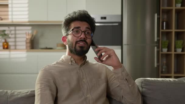 インドのアラビアの男は 家庭のキッチンで携帯電話の会話を話します 男性フリーランサー エスニック ホームオーナー スマートフォン話す オーダーフード オンライン配信 ソファーで携帯電話を話す — ストック動画