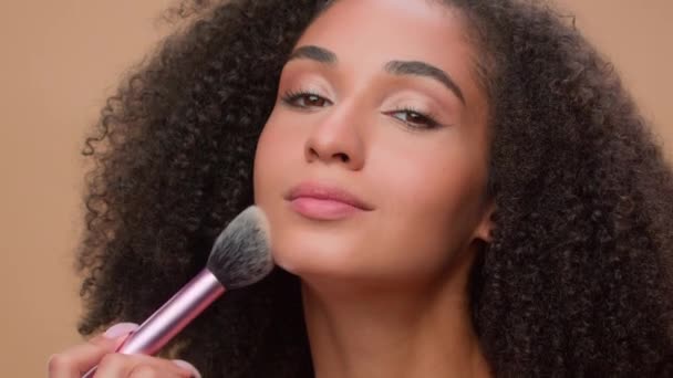 ベージュスタジオの背景美しいアフリカ系アメリカ人女性の魅力的なエスニック少女をクローズアップ化粧品の美しさのブロンザーの輪郭を準備する顔のメイクアップにパウダーを適用 — ストック動画