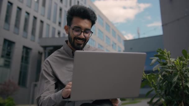 移動ショット インドのアラビアの男 笑顔のビジネスマンの雇用主 オフィスの外で街のラップトップで働く起業家 陽気なフリーランサー 考える ビジネスアイデア 遠隔教育を学ぶ — ストック動画