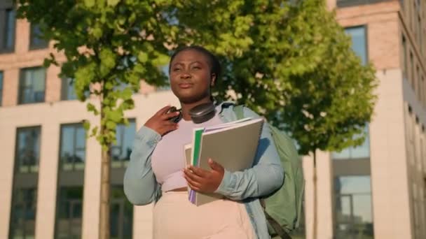 アフリカ系アメリカ人女性大学カレッジアカデミーキャンパス 学生ティーンガール高校生 学校のヘッドフォン 学校のヘッドホン 学校の授業を勉強した後 笑顔で街を歩く — ストック動画